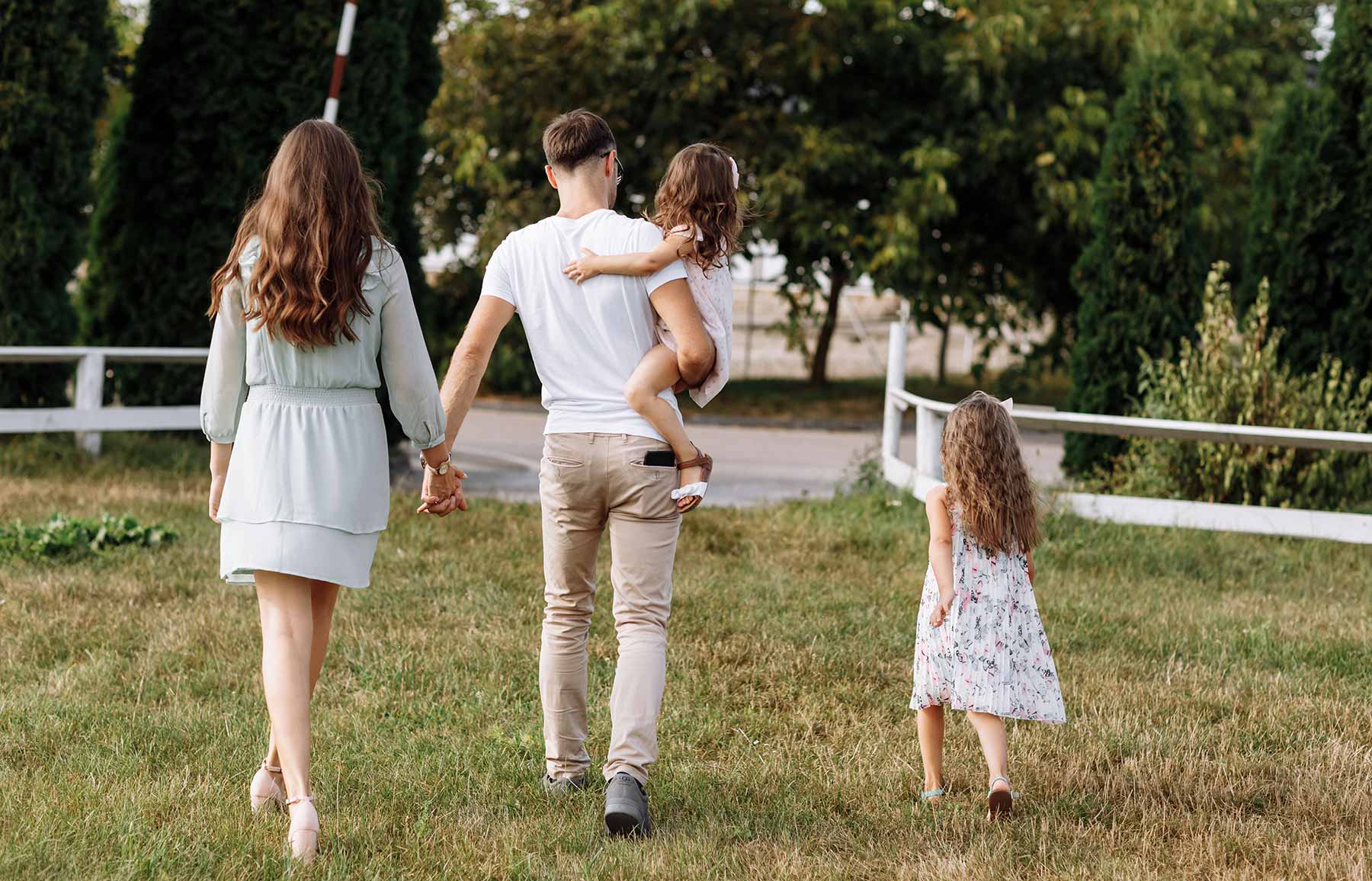 Junge Familie mit zwei Kindern geht über eine Wiese in Richtung Straße.