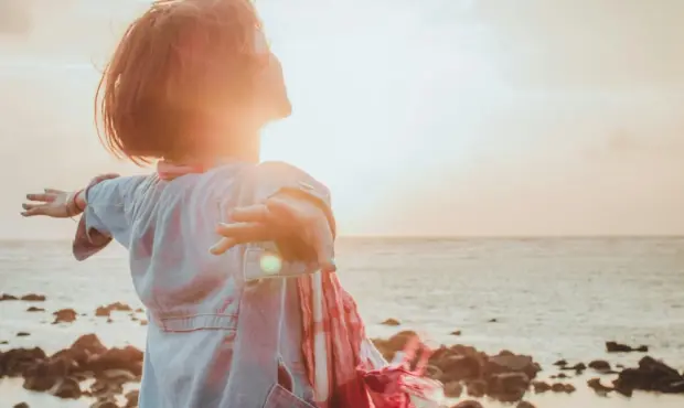 Frau breitet Arme aus und schaut Richtung Meer