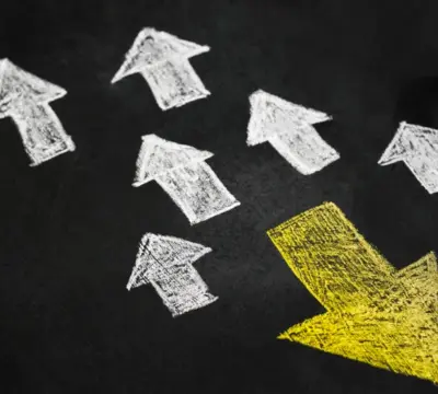 Ein gelber Pfeil zeigt in eine andere Richtung wie viele weiße Pfeile