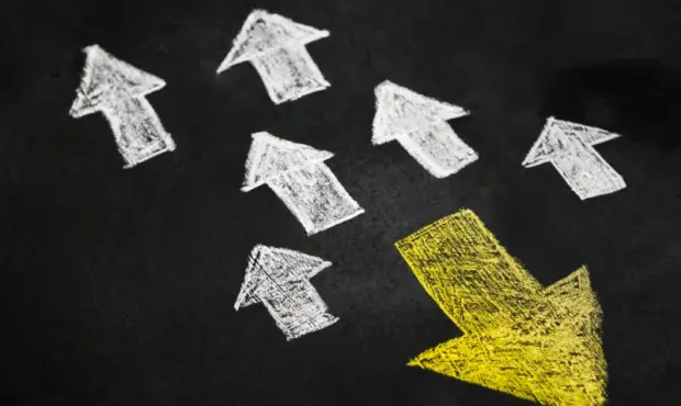 Ein gelber Pfeil zeigt in eine andere Richtung wie viele weiße Pfeile