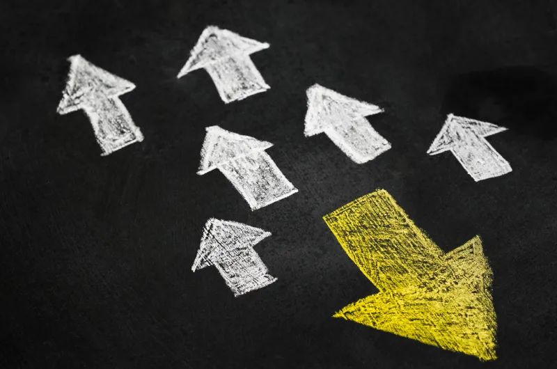 Ein gelber Pfeil zeigt in eine andere Richtung wie viele weiße Pfeile