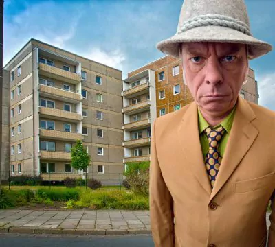 Mann in Anzug mit Hut steht vor Mehrfamilienhäusern
