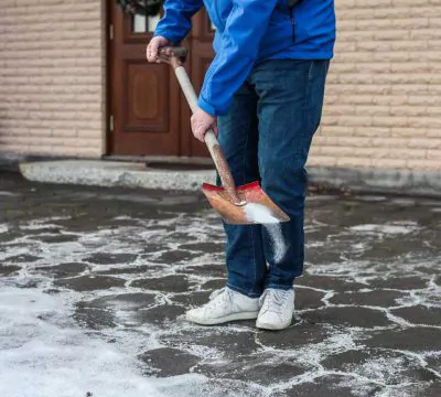 Person vor einem Haus, die mit einer Schaufel Streusalz verteilt
