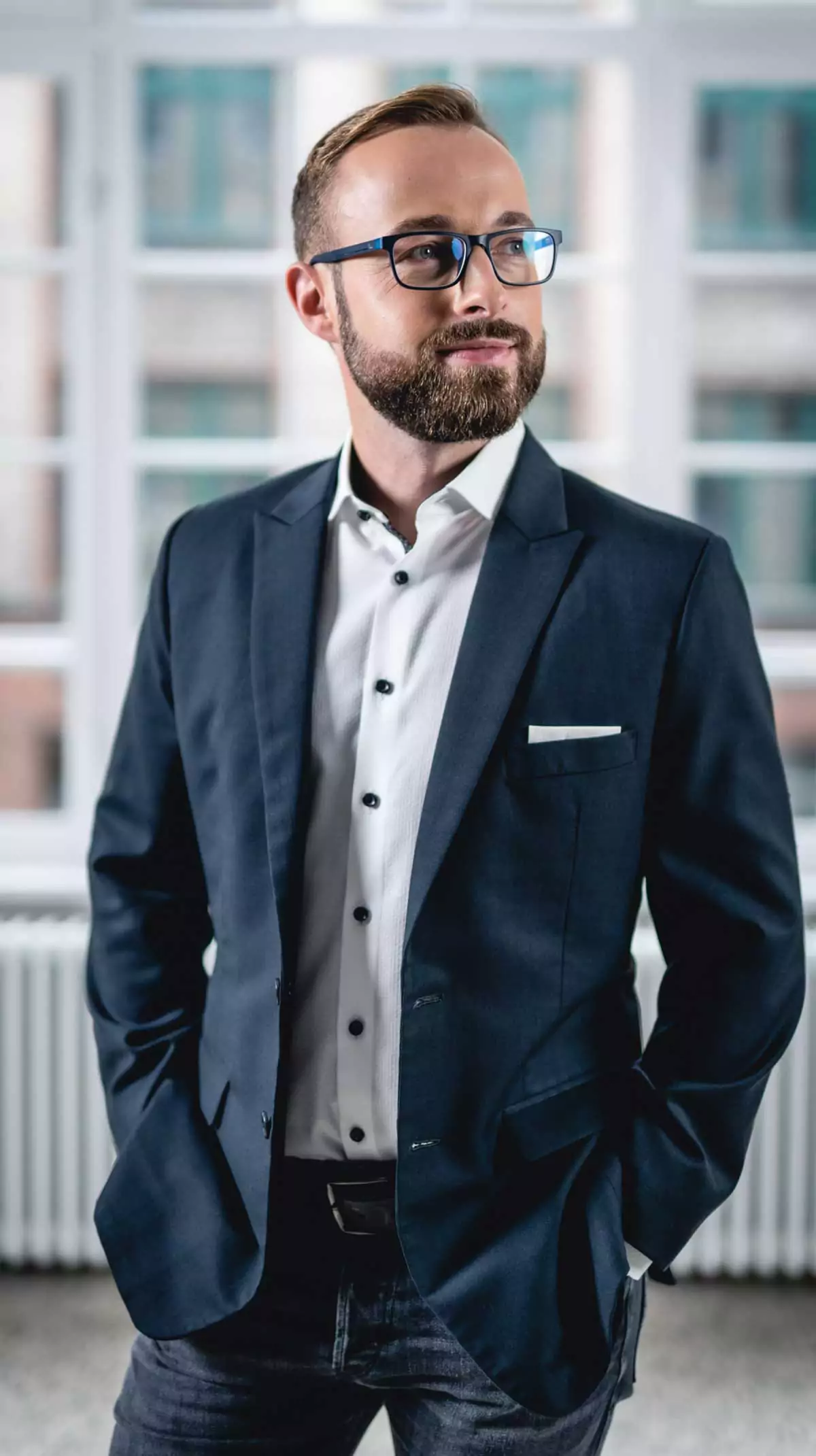 Fabian Schuster steht lächelnd zur Seite blickend vor einer Fensterfront