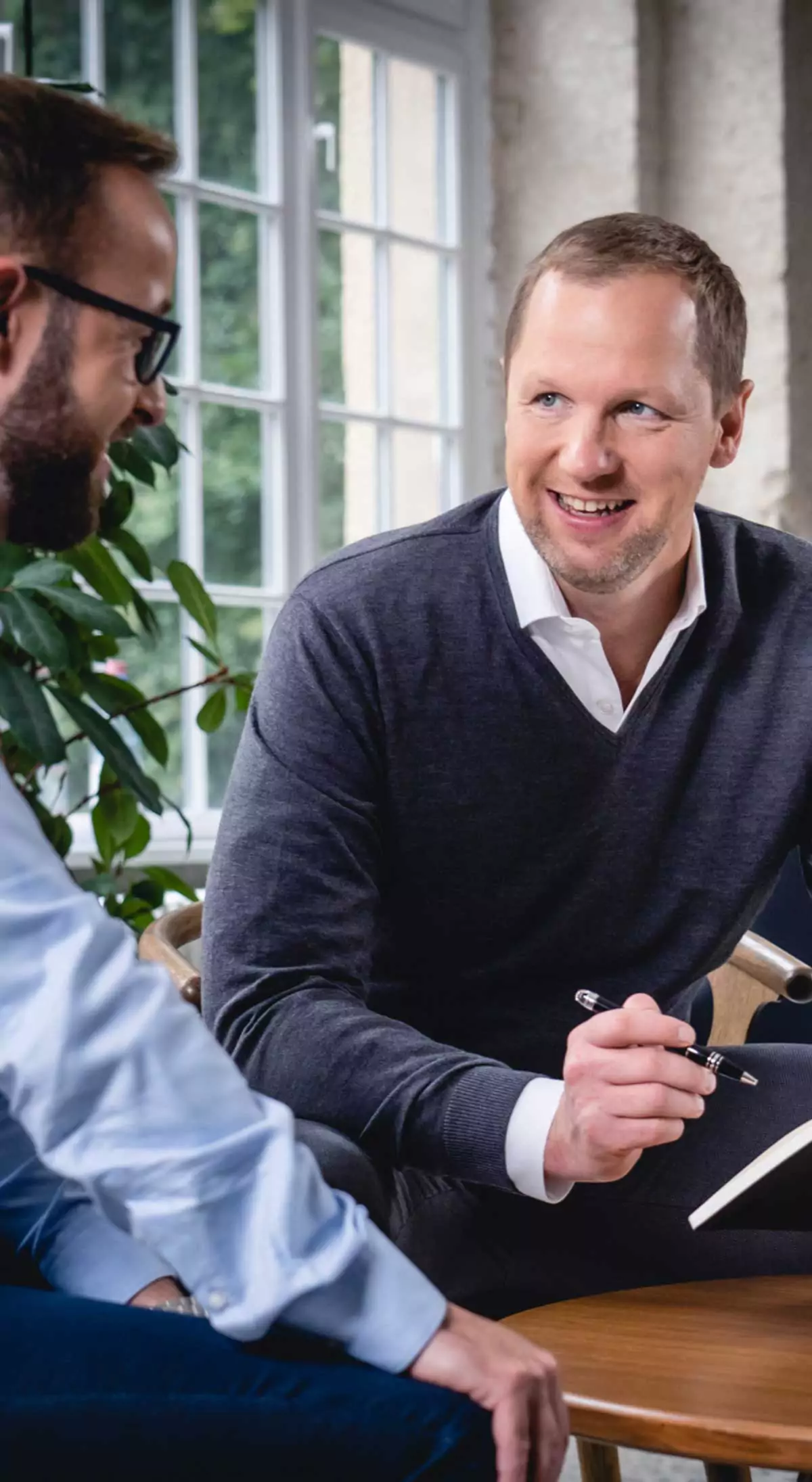 Fabian Schuster (links), Marcus Jurowski (rechts) sitzen lächelnd einander zugewandt an einem Tisch