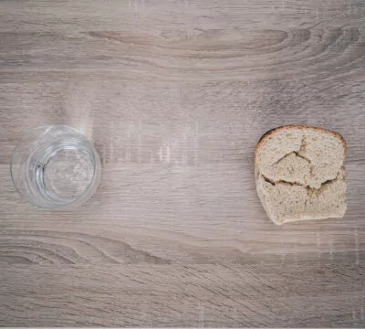 ein Wasserglas und ein Stück Brot auf Holzuntergrund