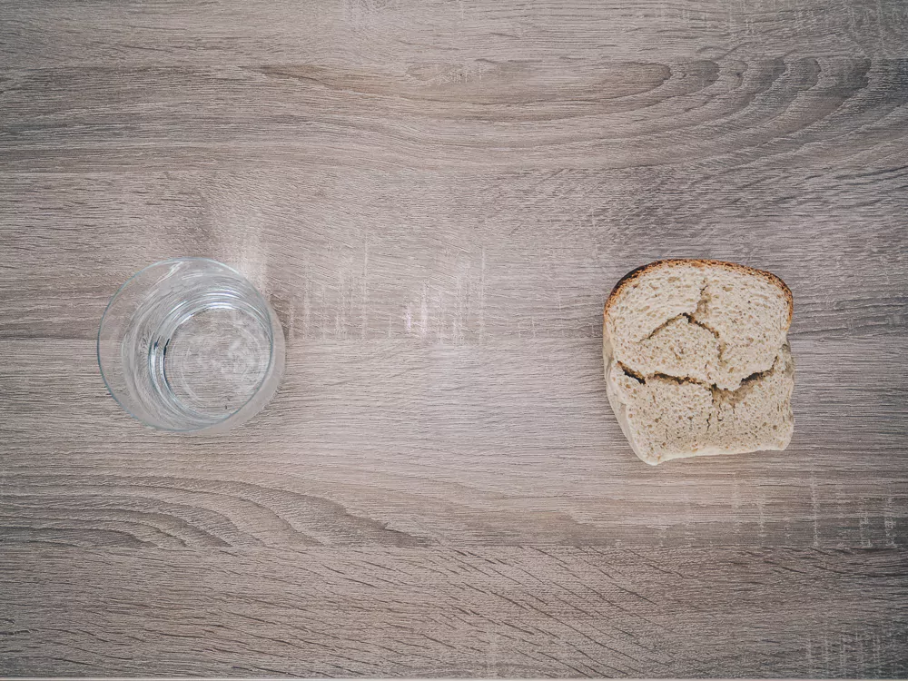 ein Wasserglas und ein Stück Brot auf Holzuntergrund