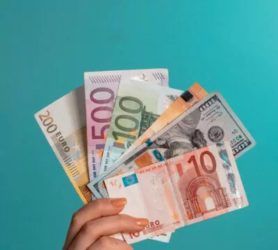 eine Hand, die verschiedene Geldscheine vor einer türkisfarbenen Wand hält