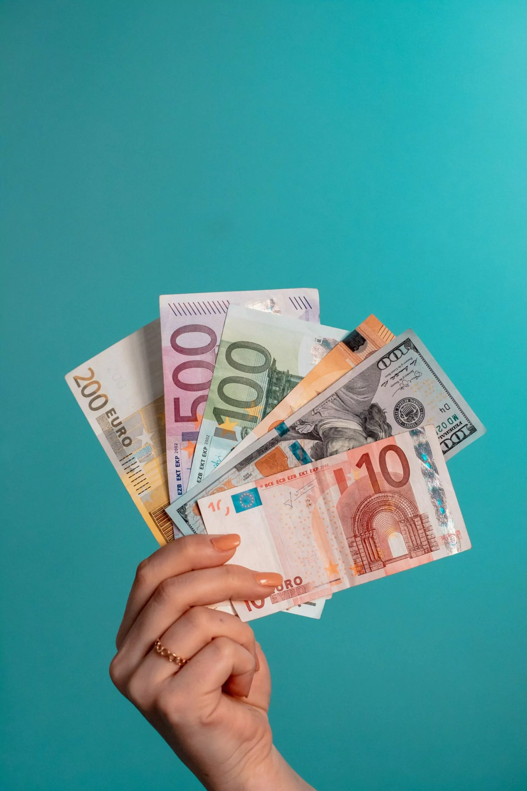 eine Hand, die verschiedene Geldscheine vor einer türkisfarbenen Wand hält