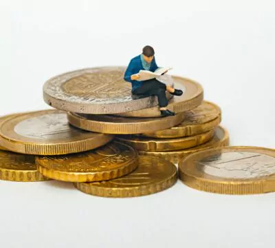 Eine Figur, die auf einem Stapel Euro-Münzen sitzt und eine Zeitschrift liest.