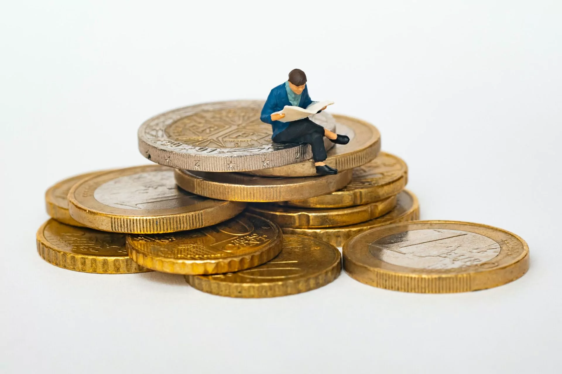 Eine Figur, die auf einem Stapel Euro-Münzen sitzt und eine Zeitschrift liest.