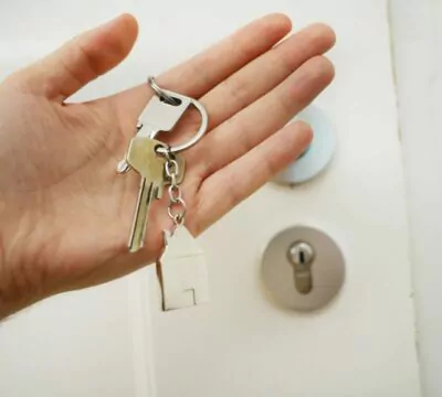 Eine Hand hält einen Haustürschlüssel, im Hintergrund die entsprechende weiße Tür.
