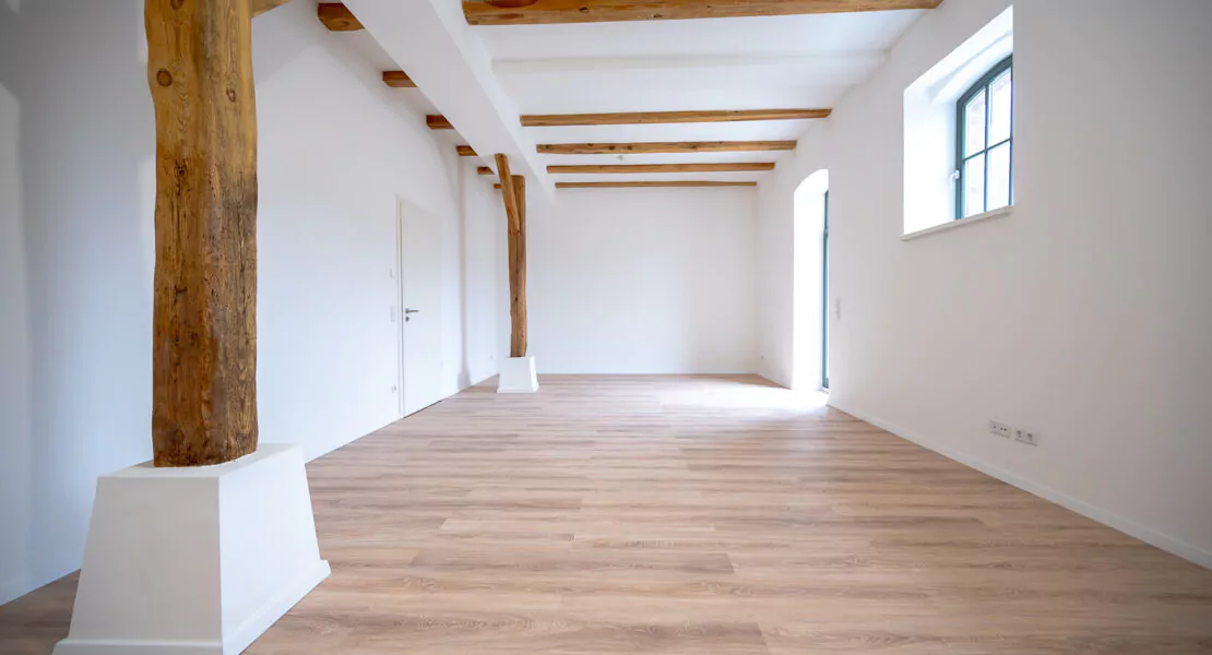 Sanierter Wohnraum mit bodentiefen Fenster, Deckenbalken und freistehenden Holzbalken