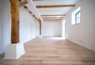 Sanierter Wohnraum mit bodentiefen Fenster, Deckenbalken und freistehenden Holzbalken