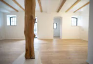 Sanierter Wohnraum mit bodentiefen Fenster, Deckenbalken und Blick auf ein weiteres Zimmer