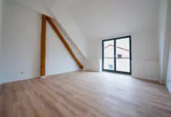 Ein leerer, sanierter Raum mit großen Fenstern und Holzbalken im Dachgeschoss