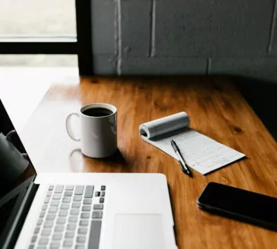 Ein Laptop, Notizzettel, Handy und Kaffee stehen auf dem Tisch