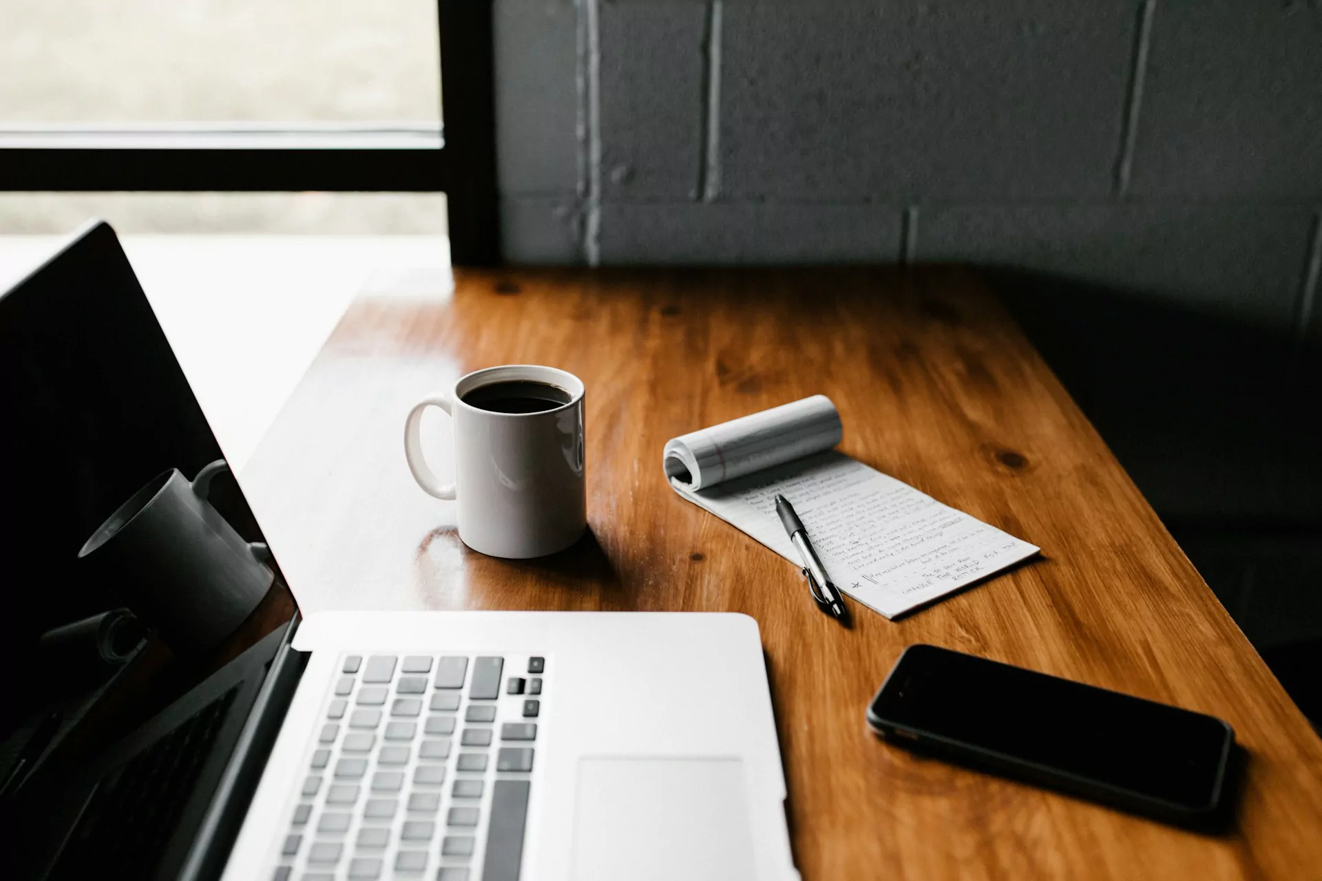 Ein Laptop, Notizzettel, Handy und Kaffee stehen auf dem Tisch