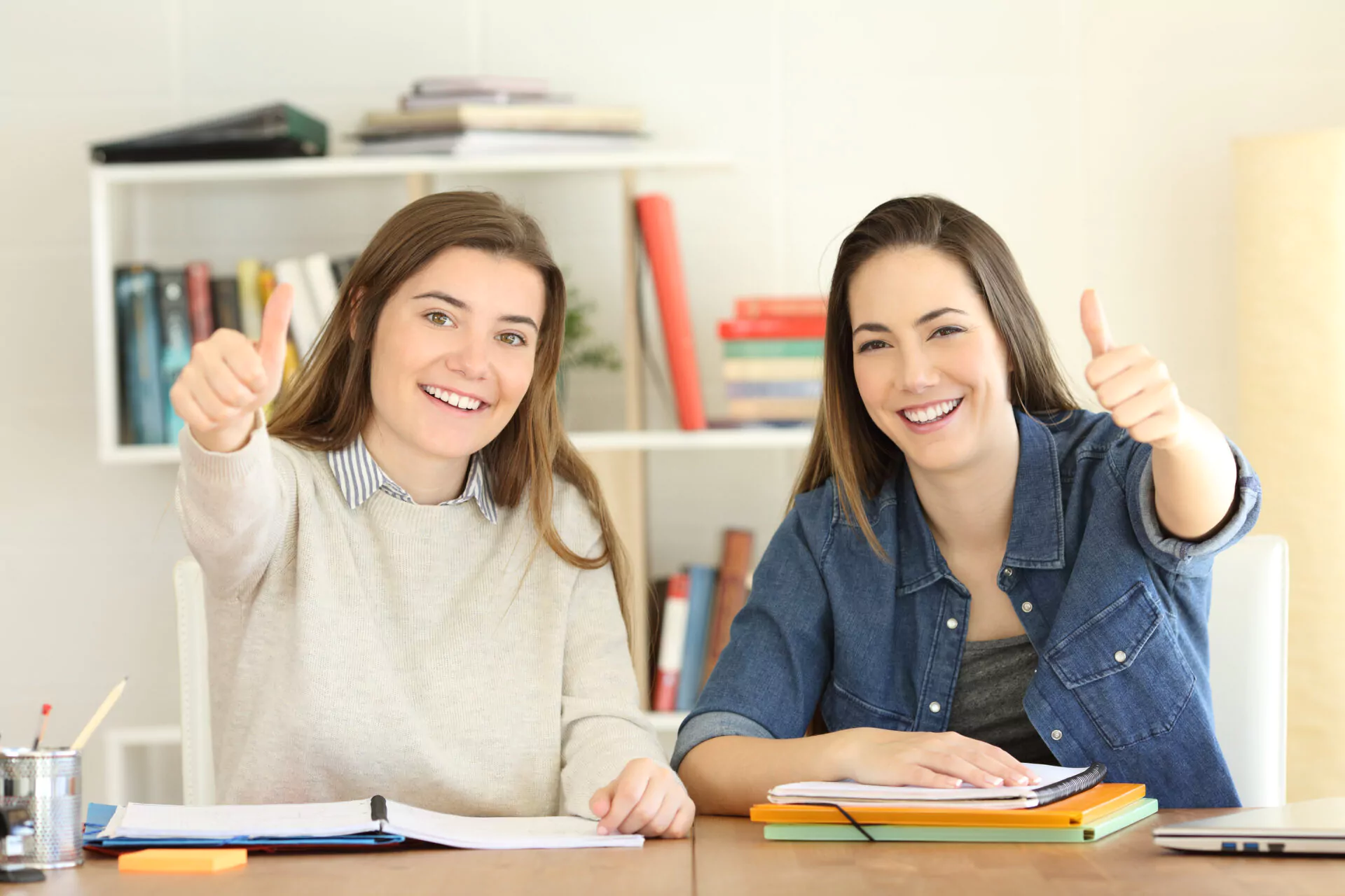 Zwei zufriedene Studentinnen zeigen den Daumen nach oben, während sie am Lernen sind