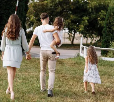 Junge Familie mit zwei Kindern geht über eine Wiese in Richtung Straße.