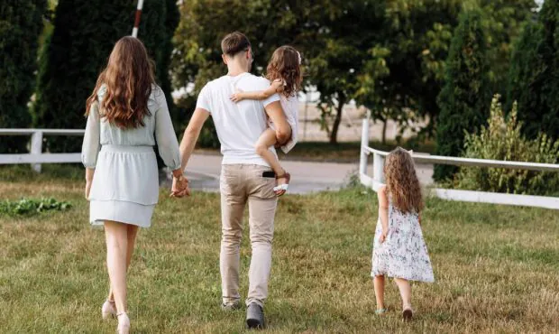 Junge Familie mit zwei Kindern geht über eine Wiese in Richtung Straße.