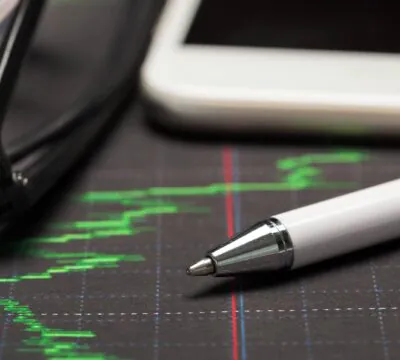 Ein Stift und ein Taschenrechner liegen auf einer Grafik der Wertentwicklung einer Geldanlage