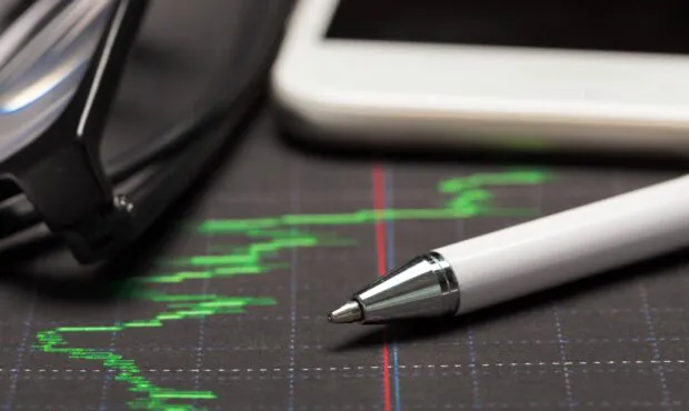 Ein Stift und ein Taschenrechner liegen auf einer Grafik der Wertentwicklung einer Geldanlage